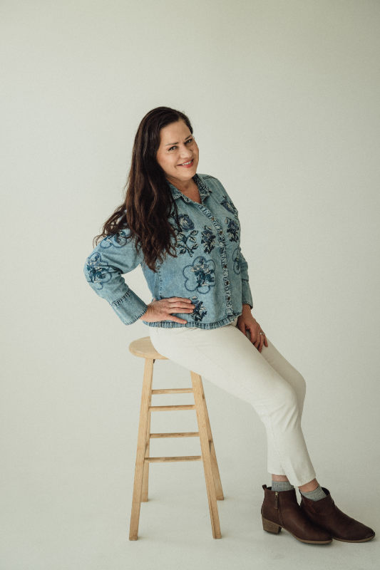 June Lemmings seated on a stool in a floral denim jacket